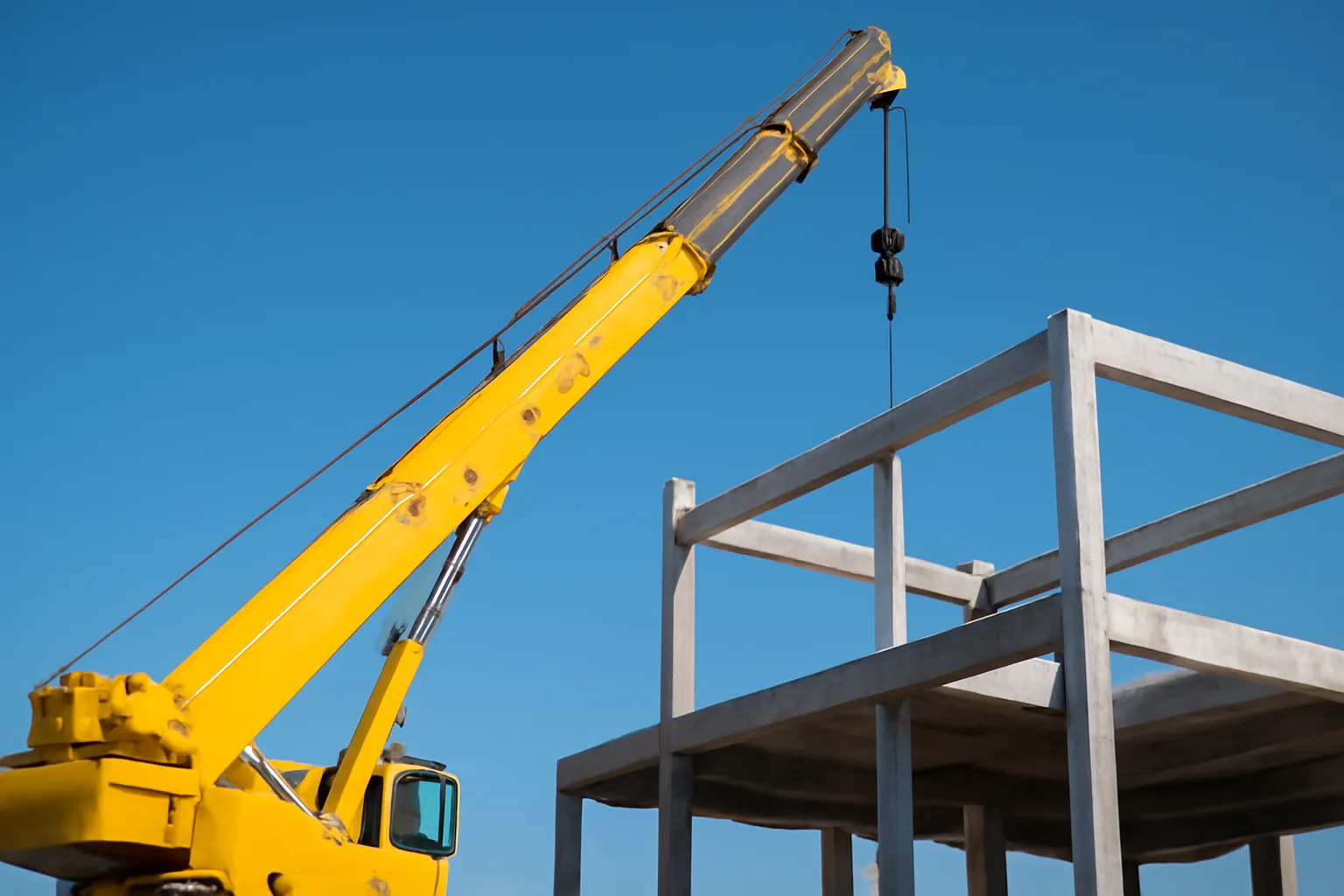 Telescopic boom crane lifting above a concrete construction frame in Arizona midday sun